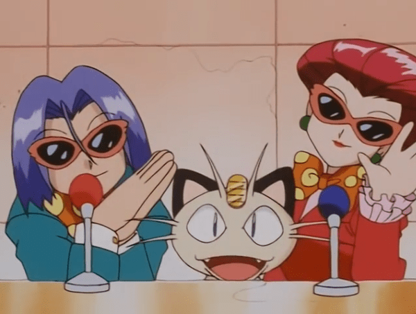 Team Rocket sitting behind microphones. Jessie and James are wearing brightly colored suits, bow ties, and sunglasses. Meowth sits between them. All three are smiling cheerfully.