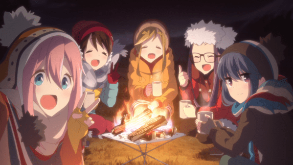A group of five teen girls in winter camping gear, sitting around a campfire and smiling at the camera as if posing for a selfie